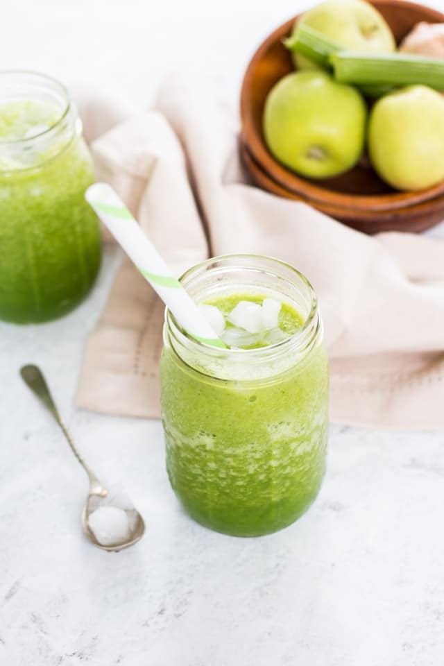 apple celery smoothie in a glass jar with a wooden bowl of apples and celery in the background