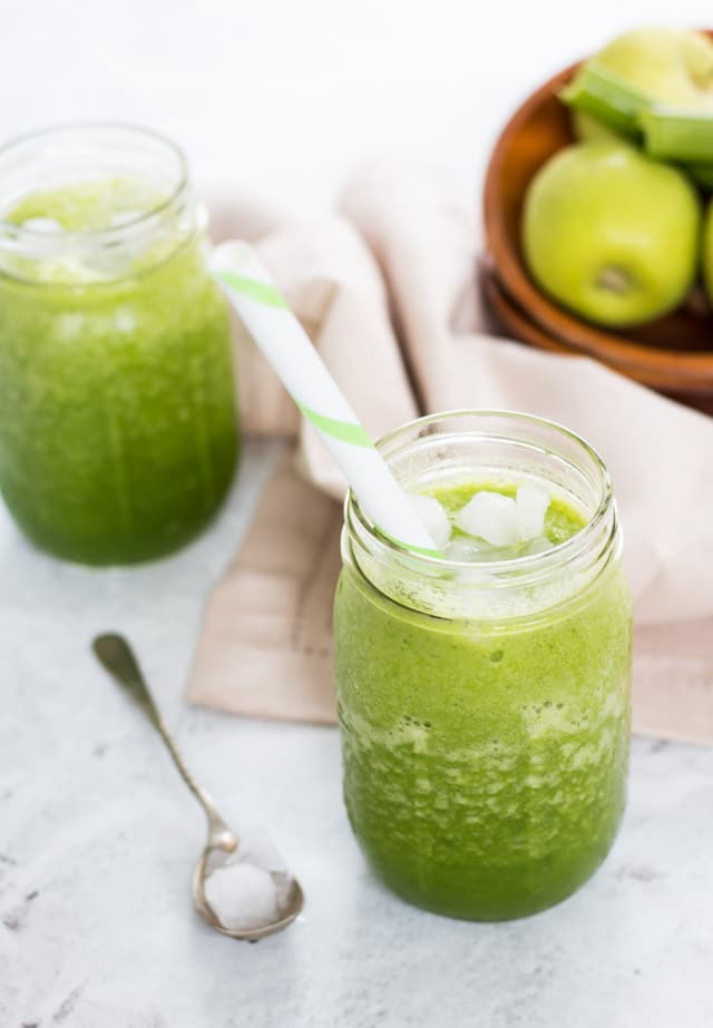 celery smoothie in a glass jar in the foreground with a bowl of apples and celery in the background