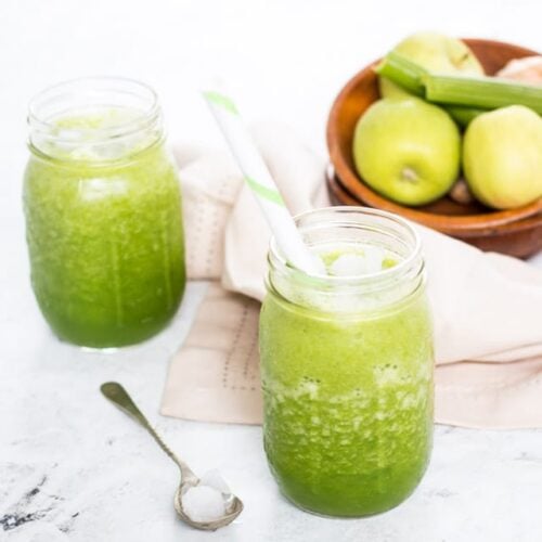 Celery smoothie in a glass jar with a wooden bowl of apples and celery in the background