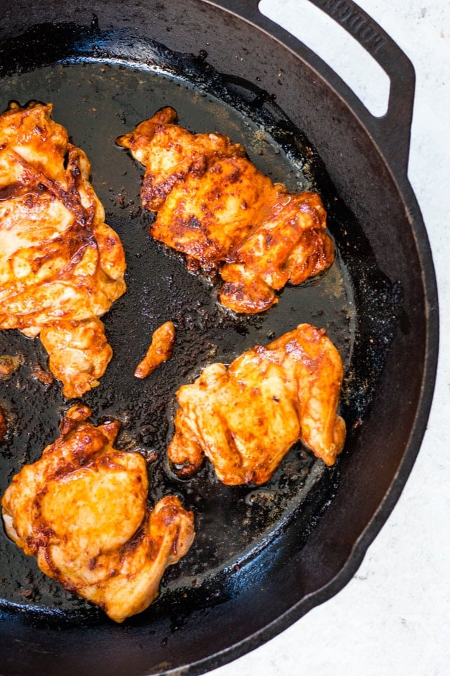 4 chicken thighs being cooked in a cast iron skillet