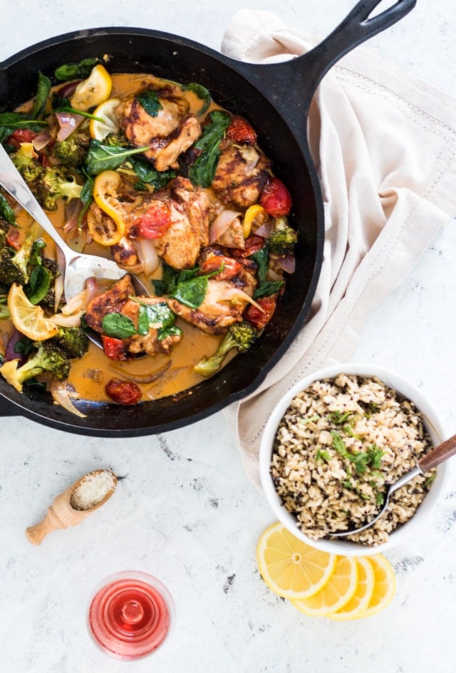 a chicken dish being served in a large black cast iron skillet with a glass of rose on the side, and a bowl of rice