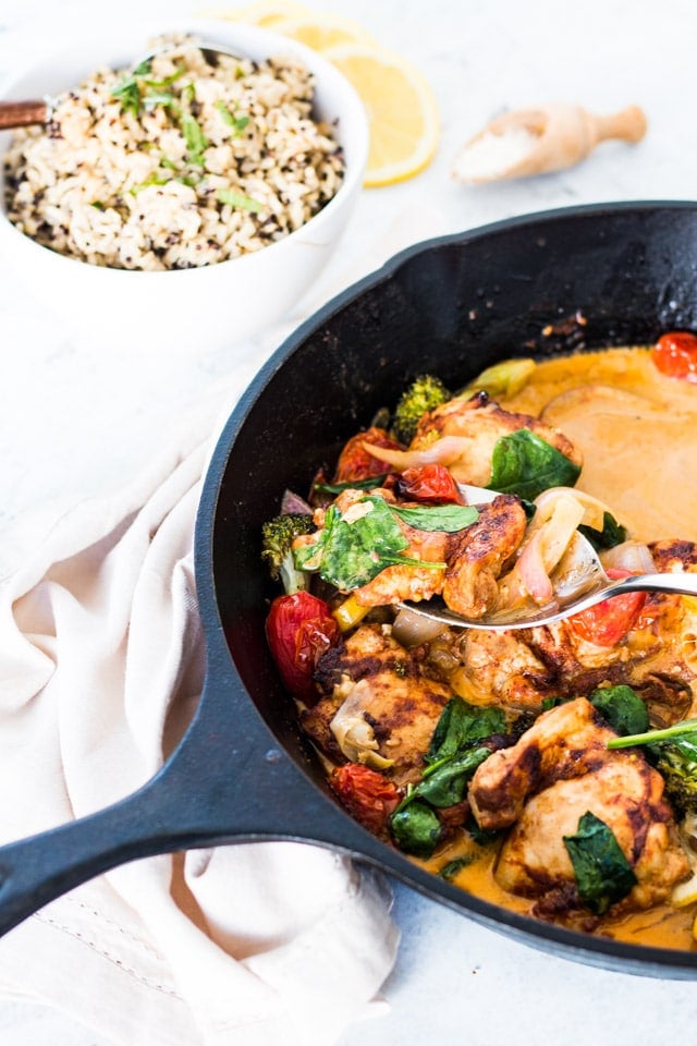 A silver spoon taking a big spoonful of lemon garlic butter chicken from a large black cast iron skillet