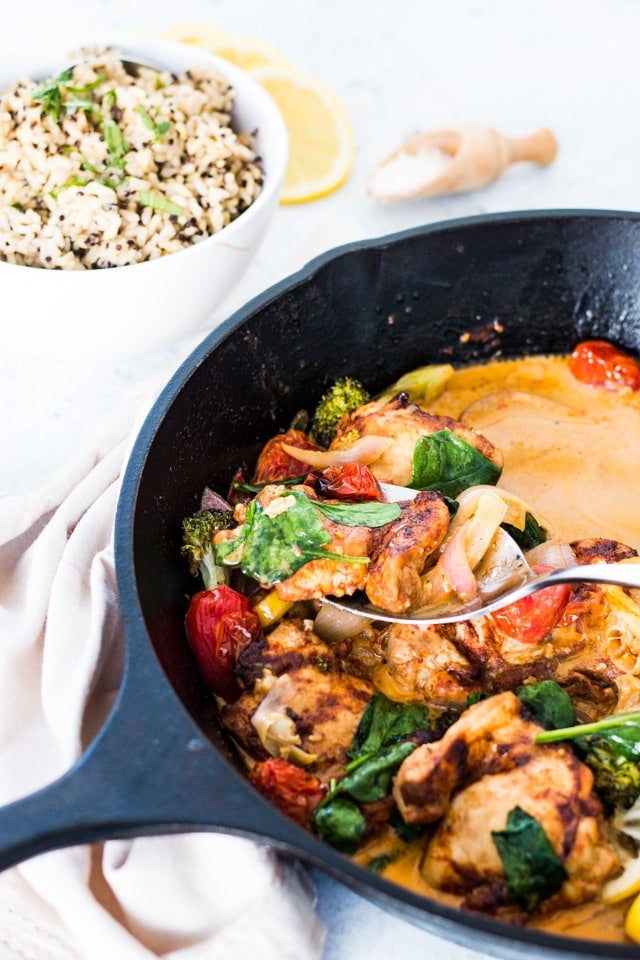 Garlic butter chicken with veggies being spooned out of a large black cast iron skillet with some rice and lemons on the side