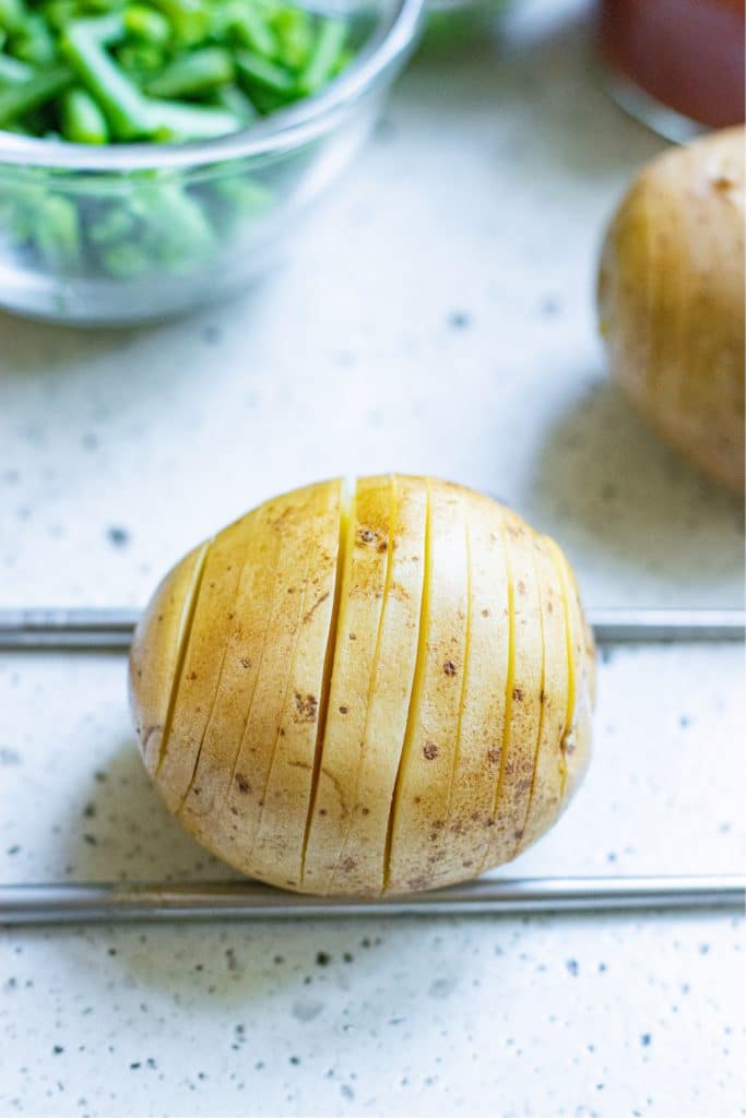 Two chopsticks placed on either side of a potato to allow for easy hasselbacking of the vegetable