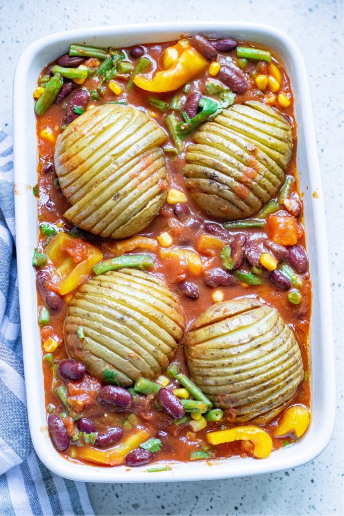 Par-cooked poatoes being placed on a casserole dish filled with chili