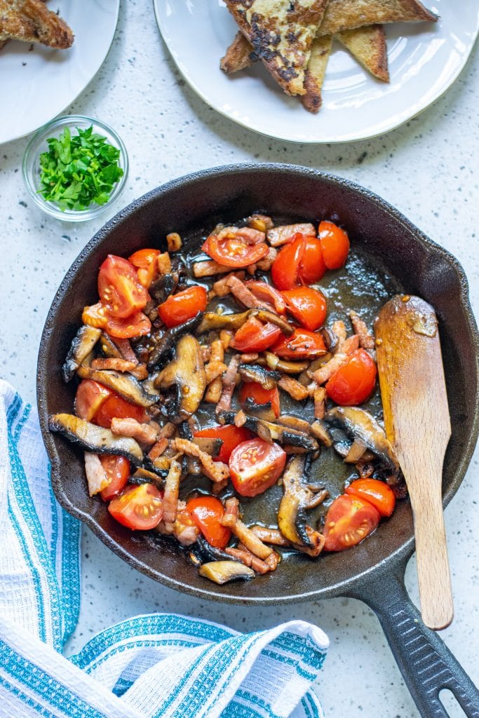 Mushrooms, bacon and cherry tomatoes being cooked in a skillet for topping savory french toast