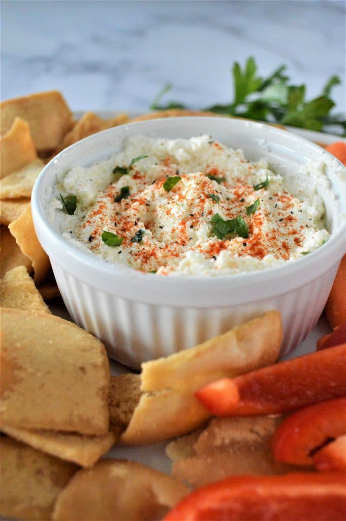 feta dip in a small white ramekin, surrounded by raw veggie sticks and pita chips