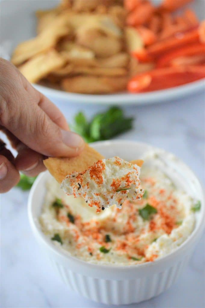Whipped feta dip in a small white bowl and some pita chips being dipped in there.