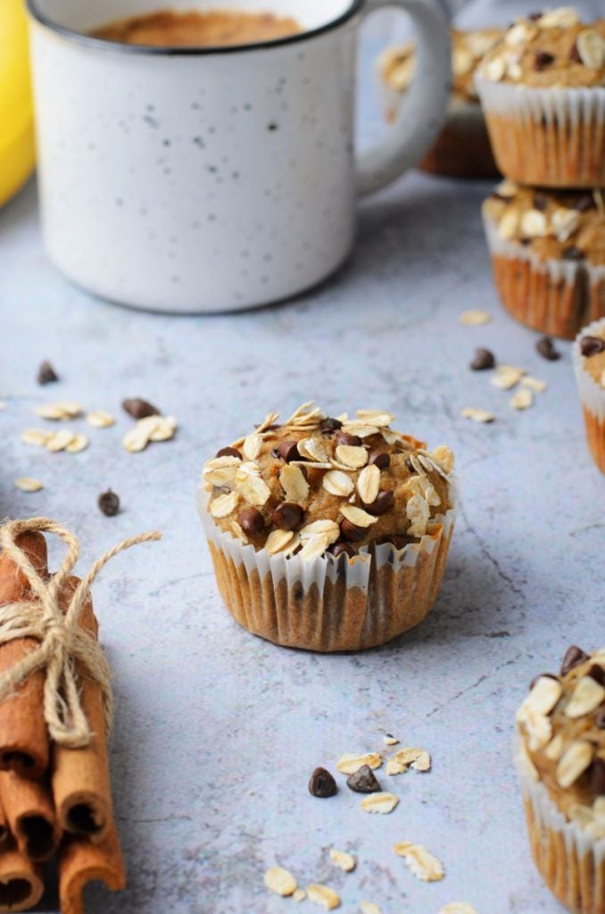 shot of Peanut butter chocolate chip banana oatmeal muffins  focused on one muffin with some extras at the side and a cup of coffee in the background