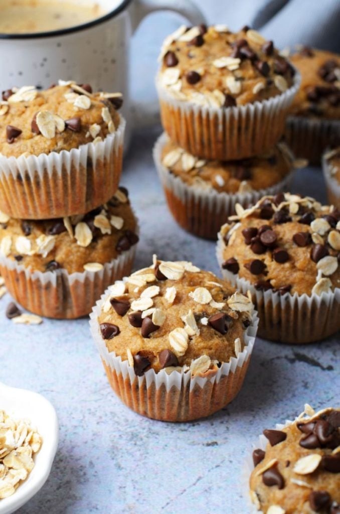 Peanut butter chocolate chip banana oatmeal muffins against a light blue background with a coffee and loose oats scattered around