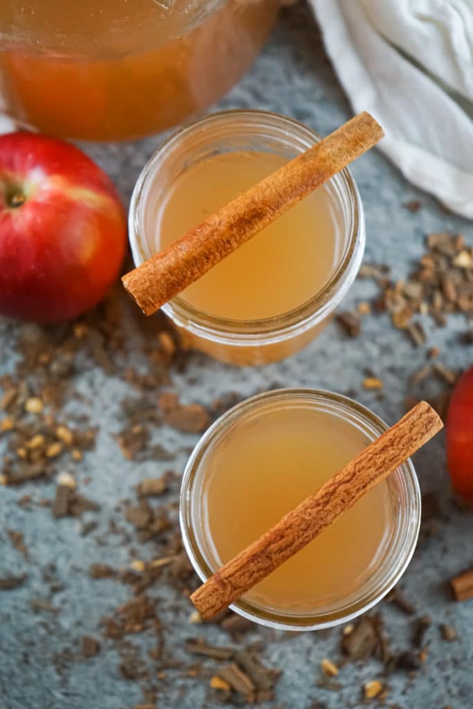 Two glasses of instant pot apple cider served in mason jars and topped with cinnamon sticks