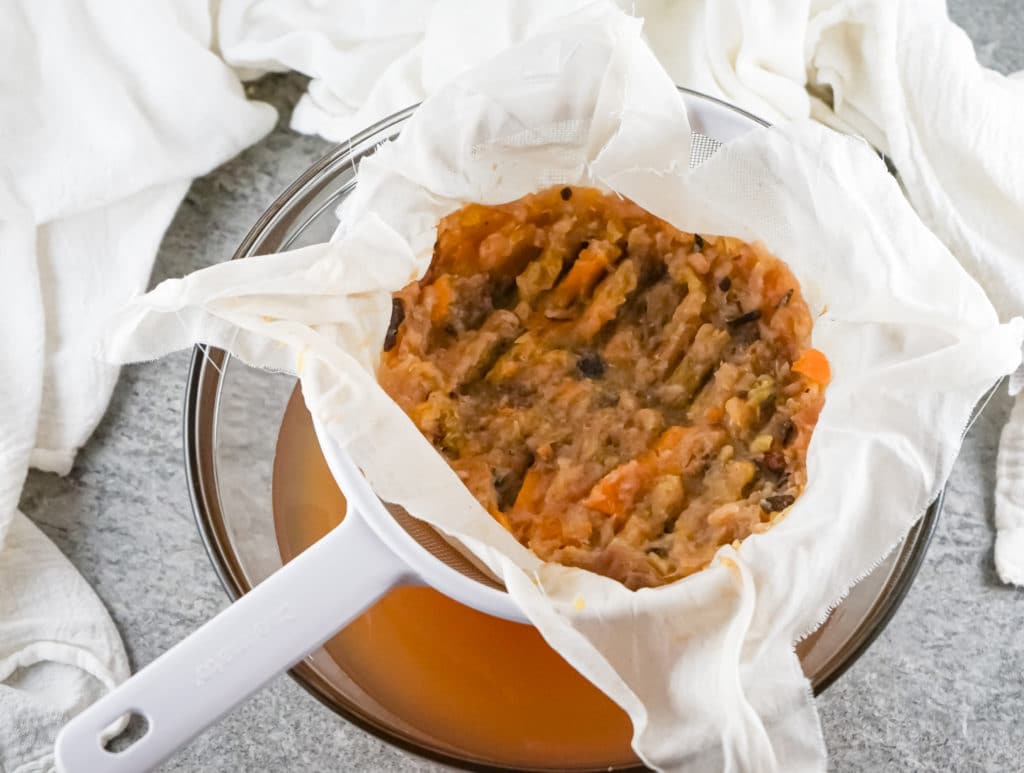 Ingredients for apple cider being mashed through a cheesecloth and strainer after being cooked in the instant pot