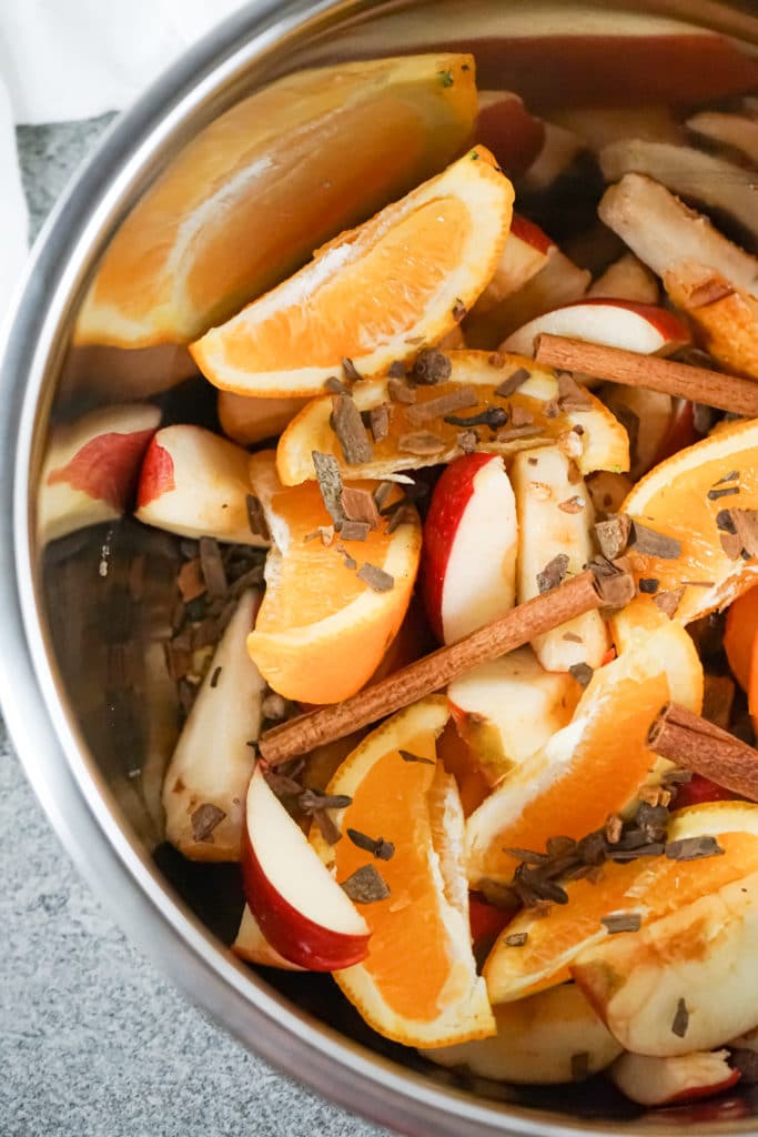 Overhead shot of apples oranges and cinnamon sticks in the bowl of a slow cooker