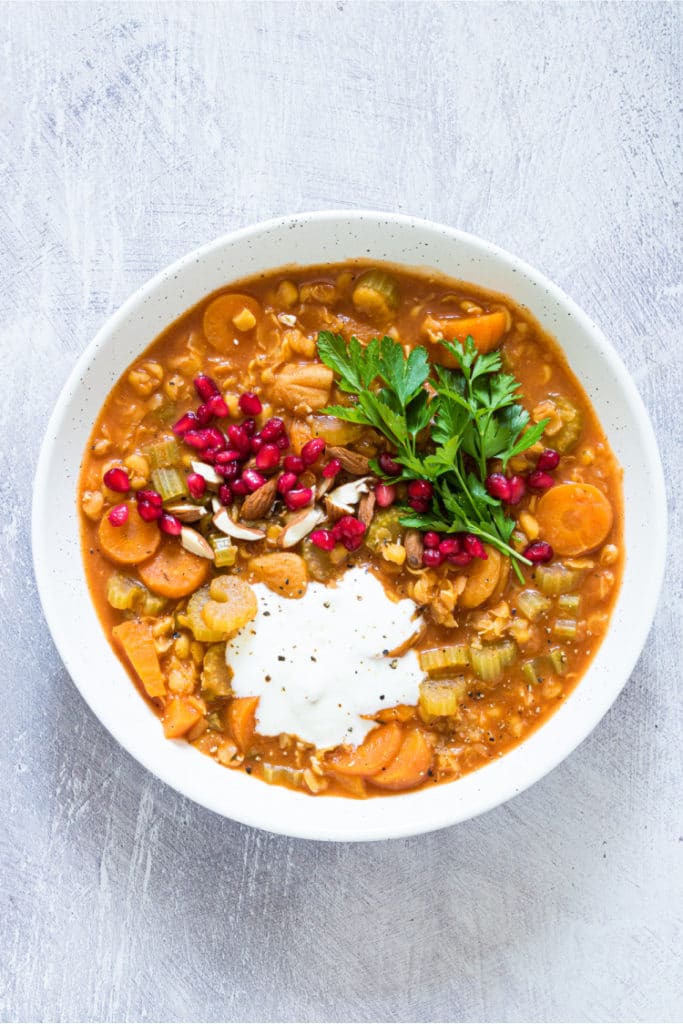 light gray background and white bowl containing split pea soup topped with yogurt and pomegranate