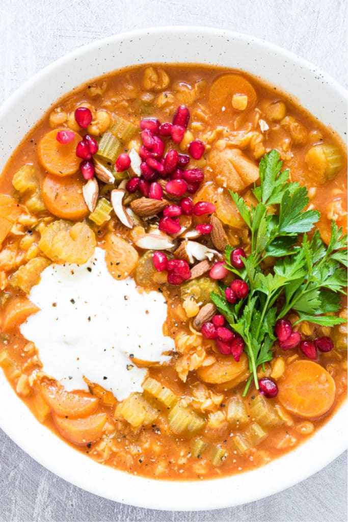 up close overhead shot of a white bowl containing a split pea soup topped with pomegranate arils and yogurt