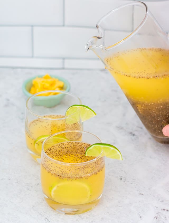 Pineapple chia fresca being poured from a large glass jug into two smaller glasses