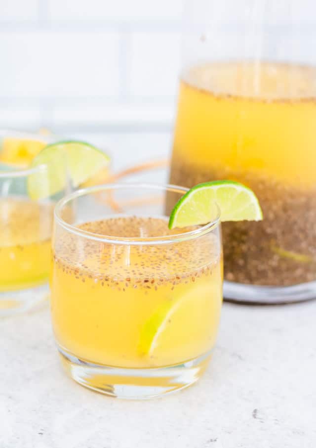 Up close shot of pineapple chia water served in a small glass with chunks of pineapple, and a wedge of lime on the side