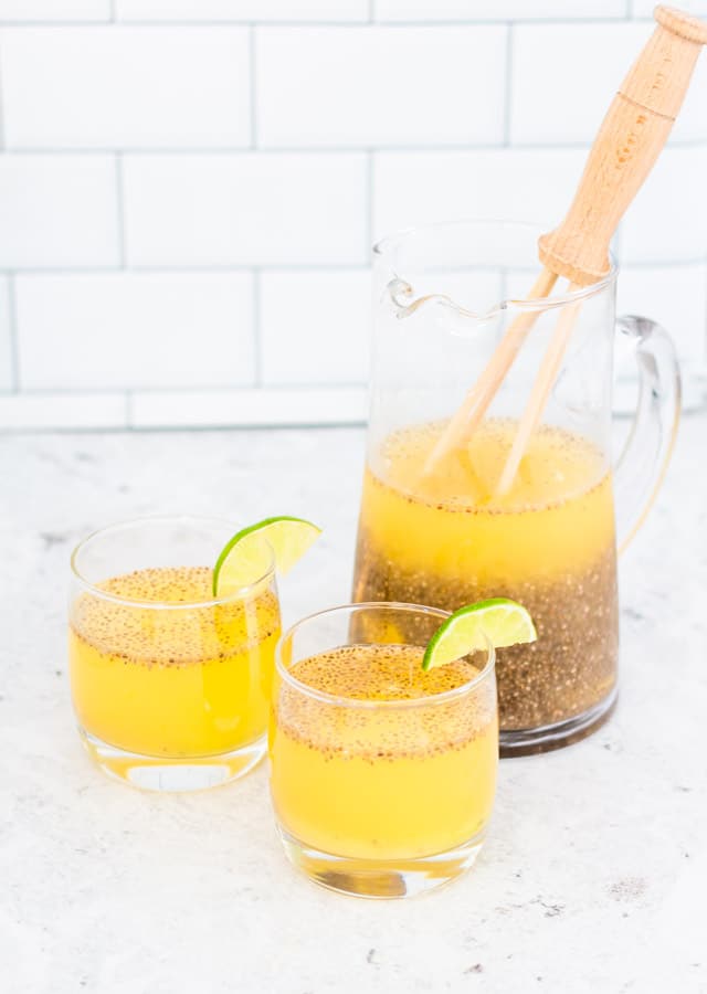 Pineapple agua fresca served in a large jug and poured into two glasses against a white background