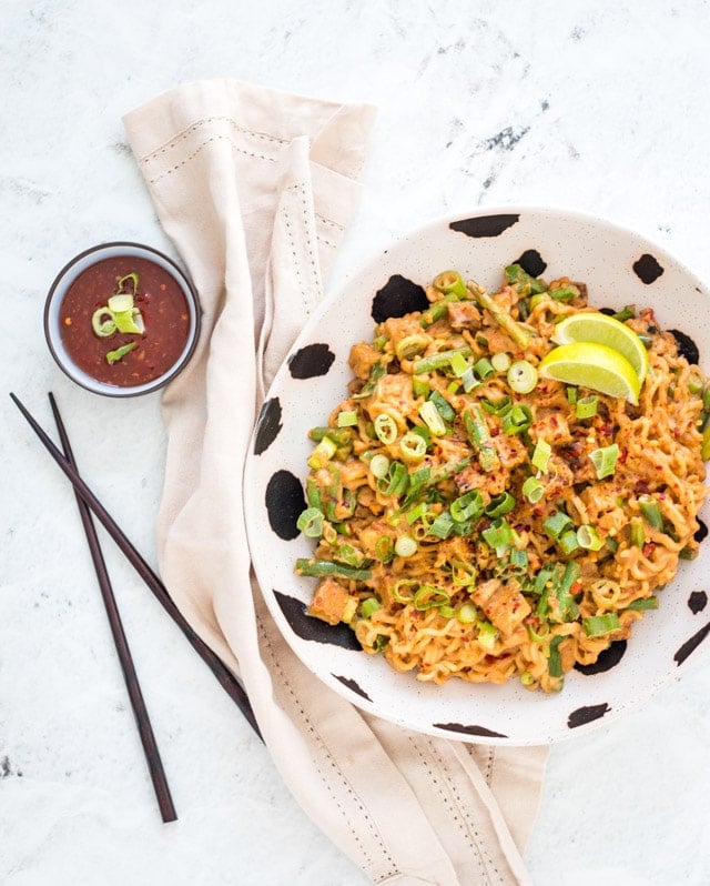 Spicy Peanut Noodles served in a black and white bowl with sweet chilli and chopsticks in the background