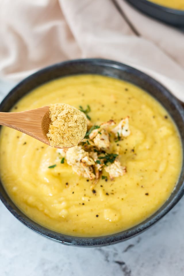 Nutritional yeast being sprinkled on top of a bowl of cauliflower soup