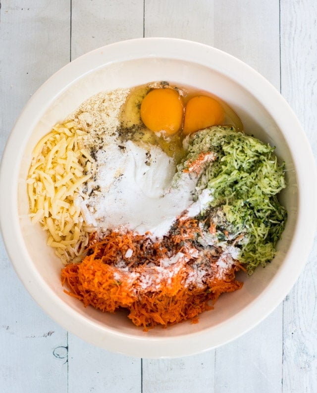 over head shot of an off-white bowl containing strained zucchini, carrrot, eggs, cheese, flour and herbs