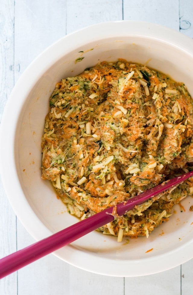 Overhead shot of an off-white bowl with the ingredients for a zucchini slice mixed together with a red spatula