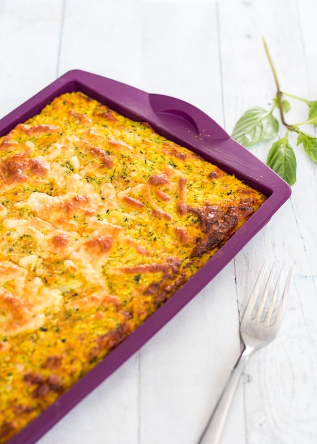 Top view of a savory slice in a purple silicone baking dish against a white background with some basil and a fork