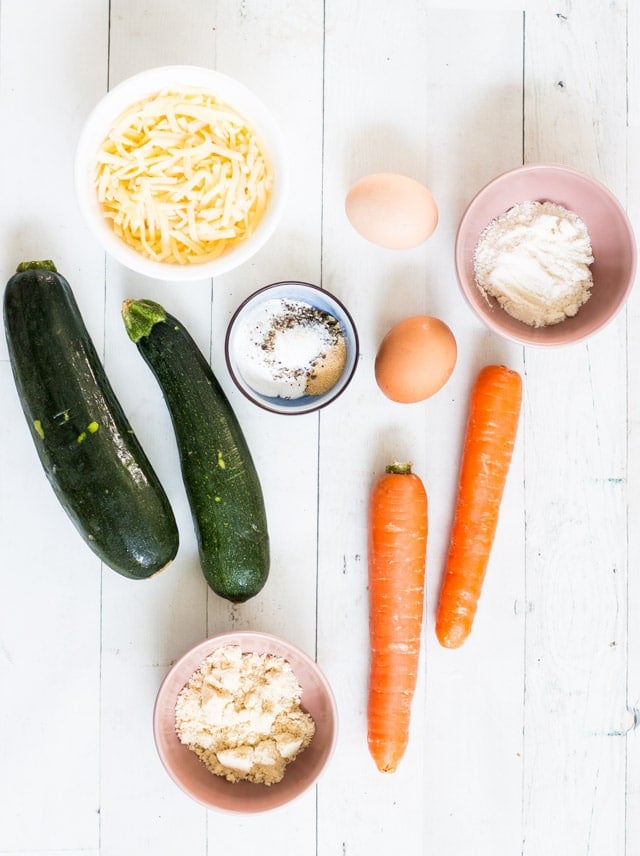 overhead flatlay shot of zucchini, carrot, egg, cheese and small bowls with herbs and flour