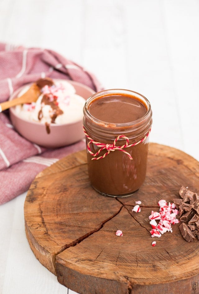 chocolate cream stored in a glass mason jar with a bowl of ice cream in the background and some of the sauce drizzled on