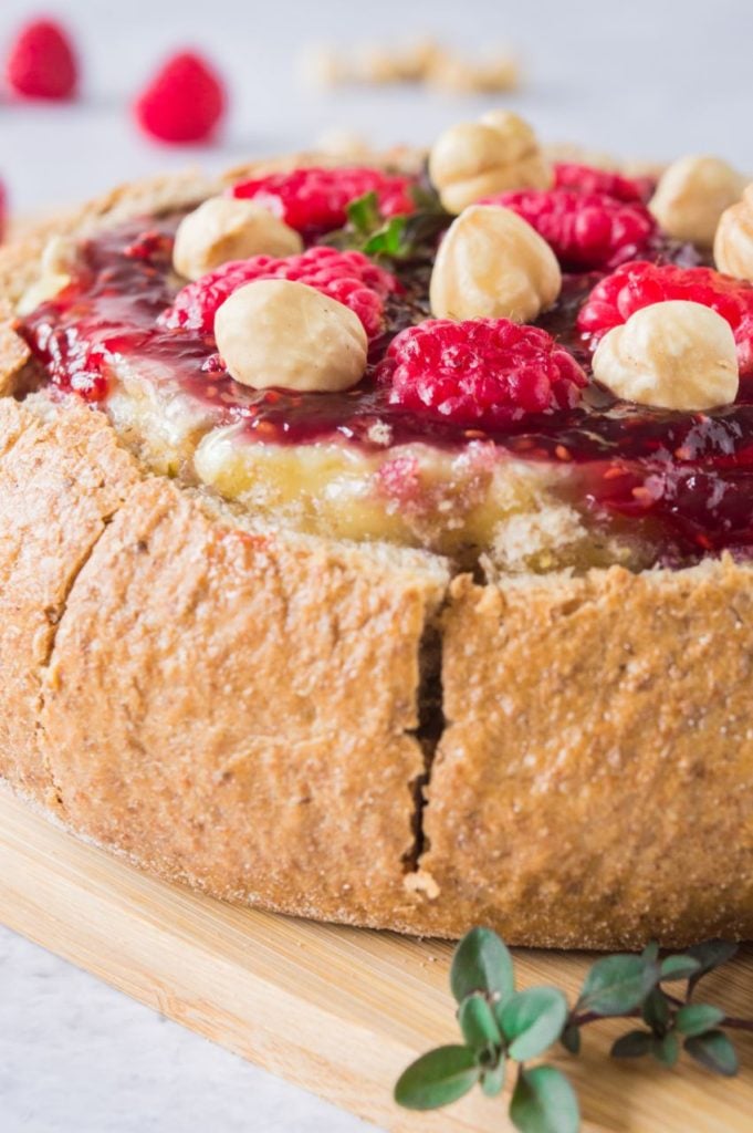 Baked brie in a whole meal cob loaf topped with raspberries and hazelnuts on a wooden board