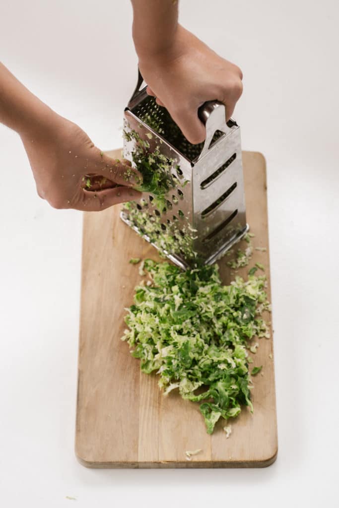 Side view of a box grater being used to grate brussels sprouts