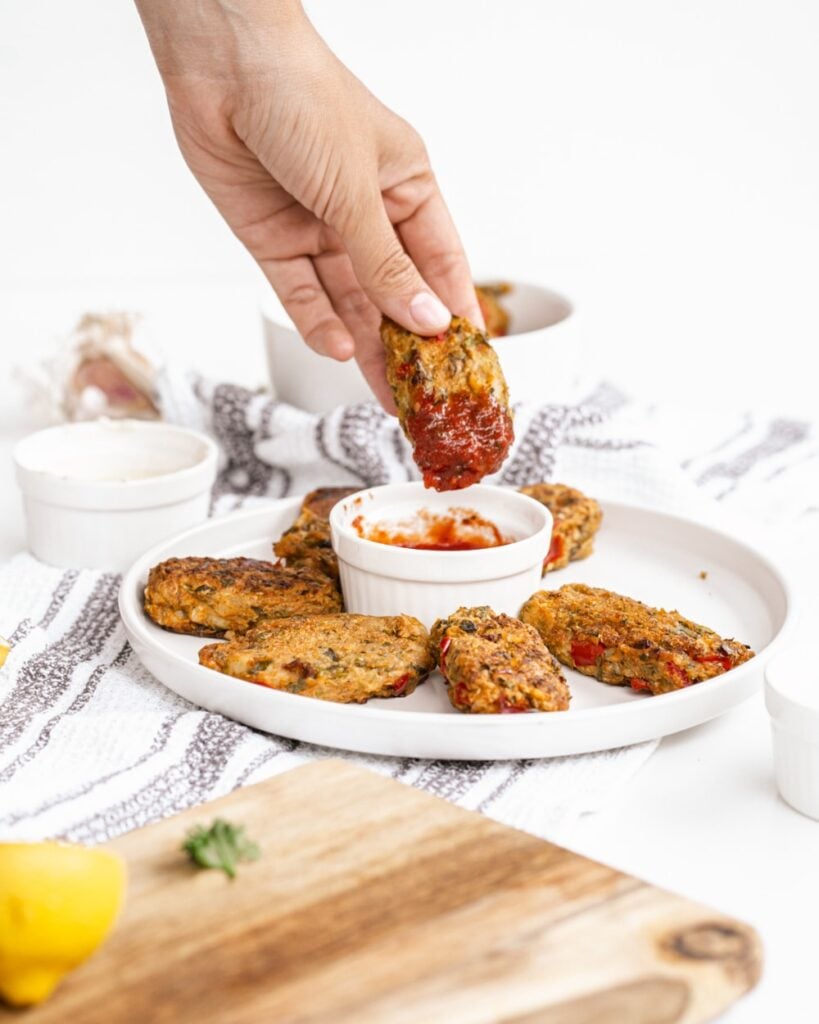 veggie loaded tater tots laid out on a white plate with one being dipped into tomato ketchup