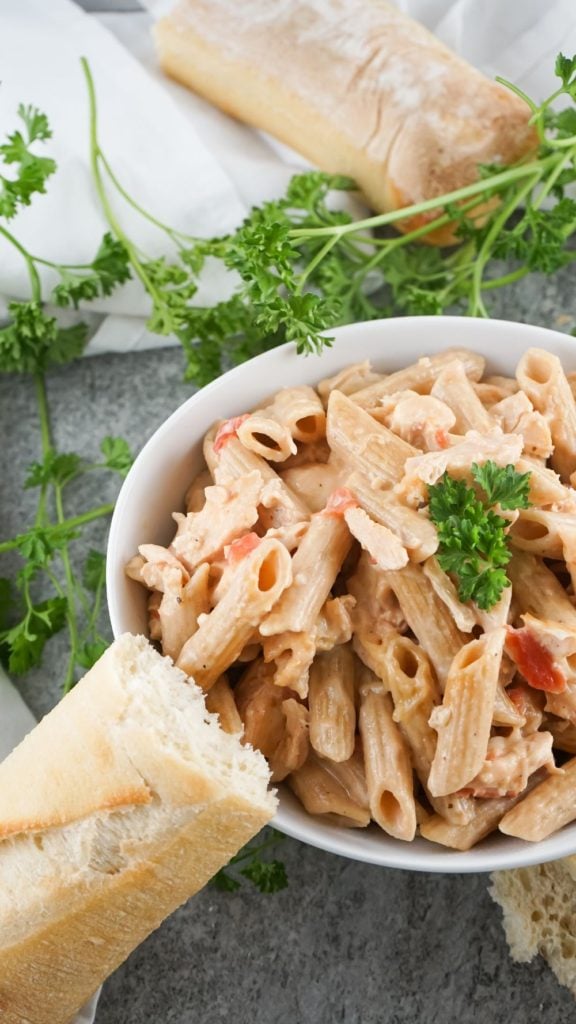 Alfredo chicken pasta bake served in a white bowl with some crunchy bread on the side