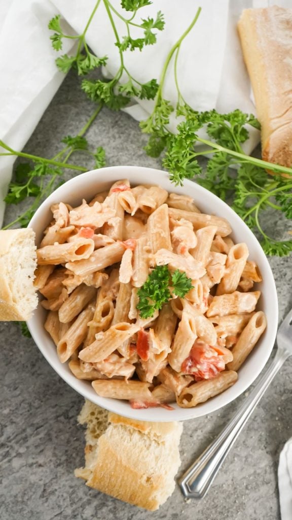 overhead shot of a bowl of creamy pasta served in a white bowl with some crunchy bread and parsley on the side