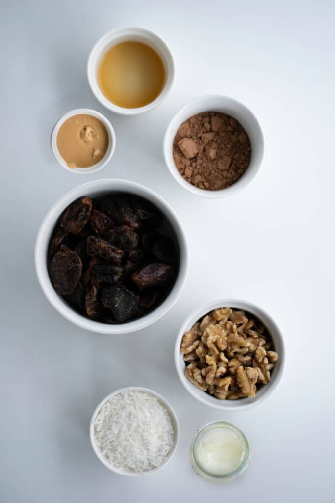 Overhead shot of ingredients for vegan no-bake brownies in white bowls against a white background