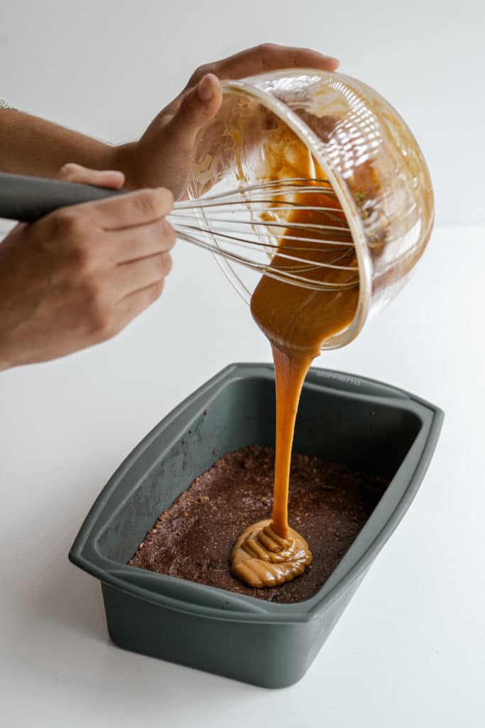 Peanut salted caramel sauce being board on top of a no-bake brownie base