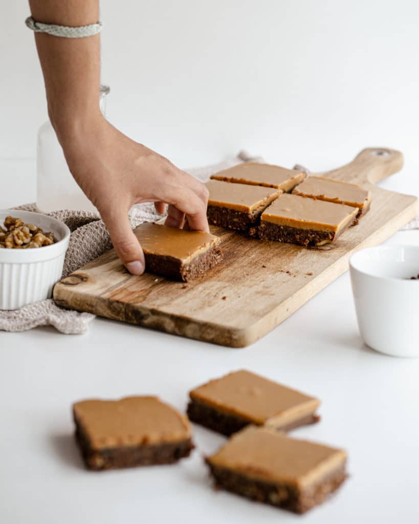 A hand lifting a slice of a vegan brownie from a wooden chopping board