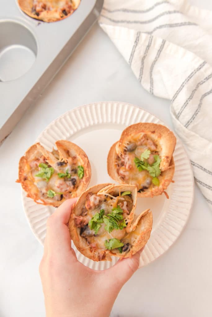 overhead shot of beef enchiladas baked in muffin tin tortillas and topped with cilantro and being picked up by a hand