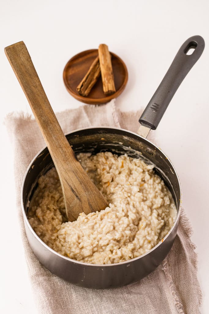 almond milk rice pudding in a saucepan being stirred with a wooden spoon