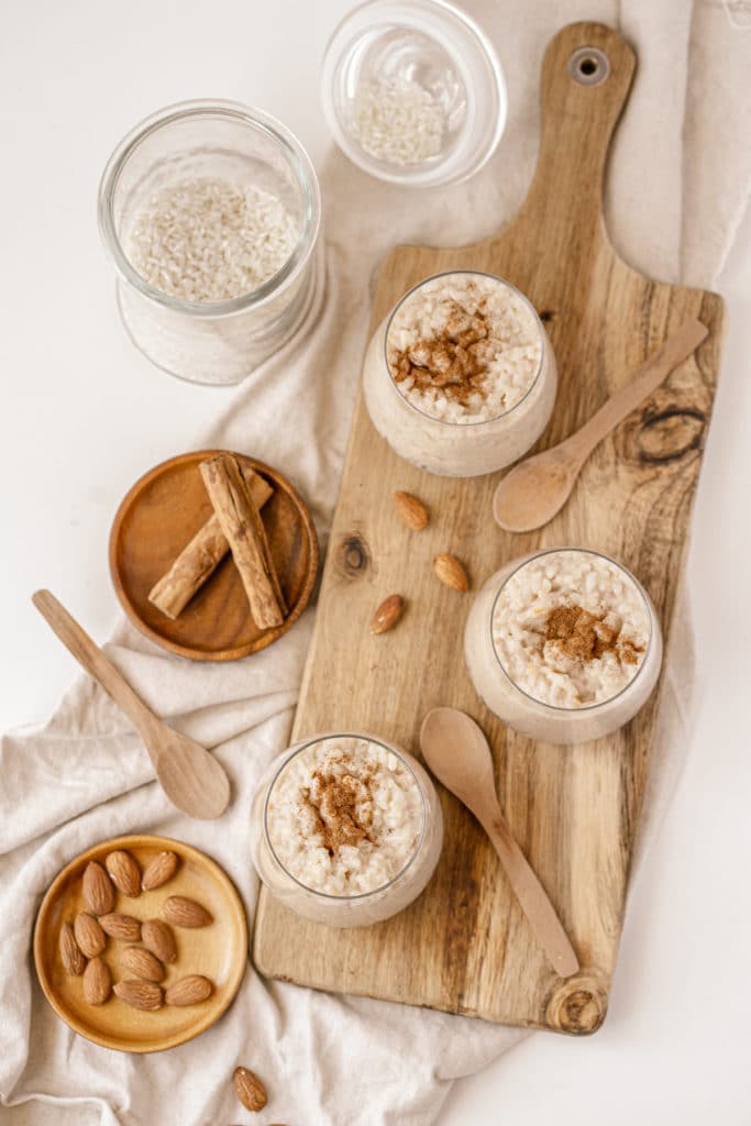 Easy almond milk rice puddings served in gold and white tea cups on wooden boards with extra cinnamon and almonds in the background