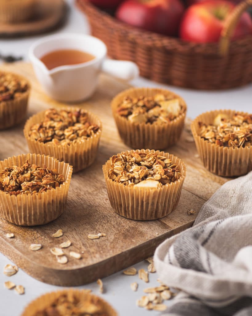 wooden board containing apple cinnamon oatmeal cups with fresh apples and honey in the background