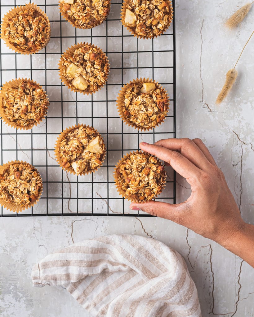 overhead shot of a hand reaching for a baked apple cinnamon oatmeal muffin on a cooling rack