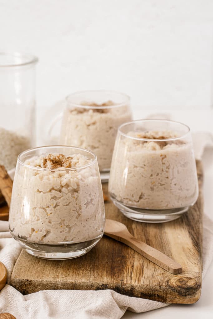 Glasses of stovetop rice pudding served on top of a wooden board and topped with extra cinnamon and almonds