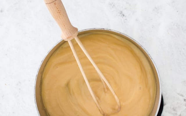Overhead shot of lemon curd in a small saucepan being whisked by a wooden whisk