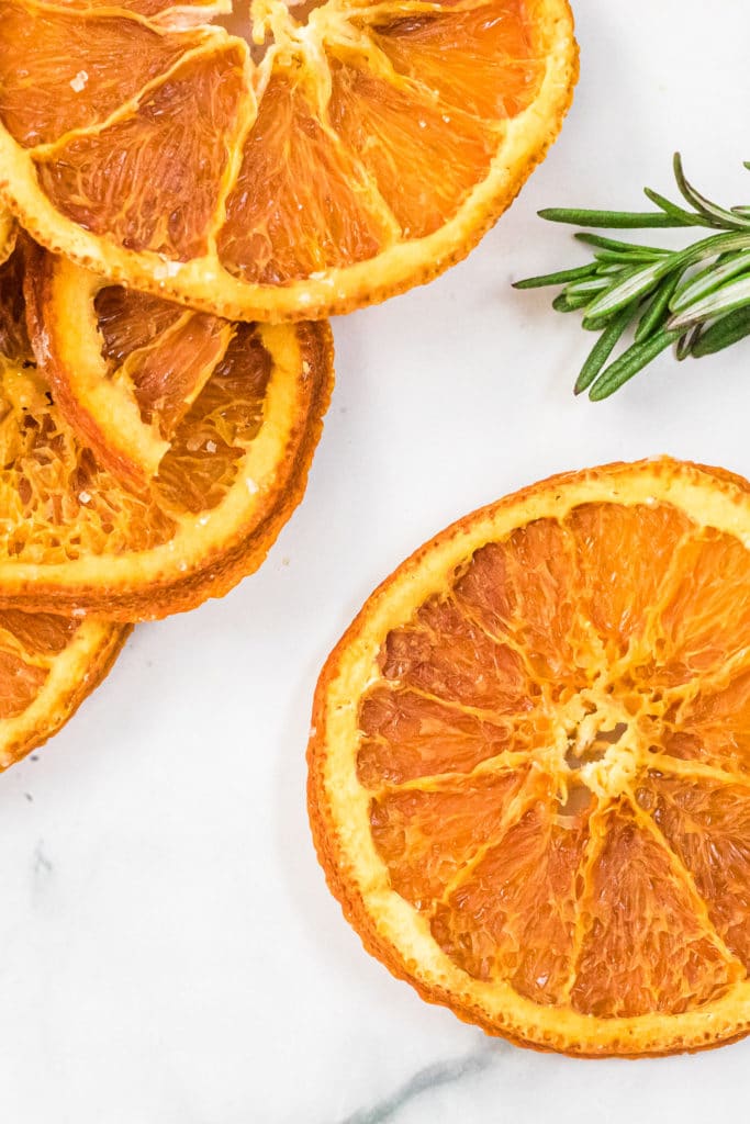 overhead shot of dehydrated orange slices with a sprig of fresh rosemary against a white background