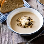 bowl of potato and leek soup served on a wooden table with some fresh bread on a linen napkin in the background