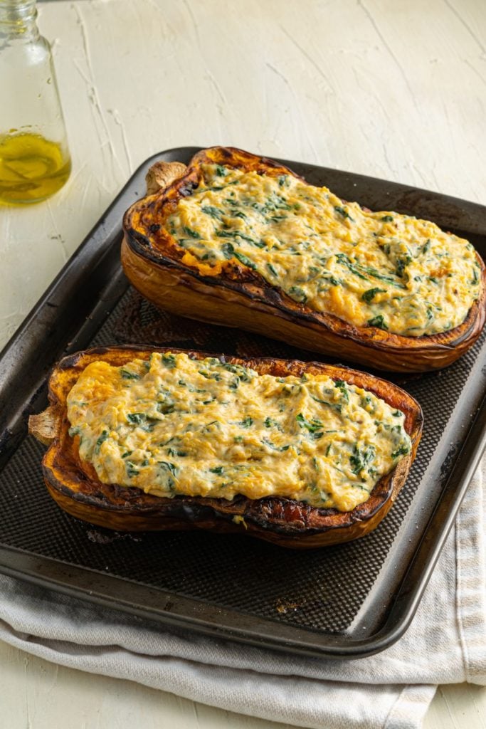 Roasted and stuffed butternut squash on a baking tray to be baked until the cheese has melted