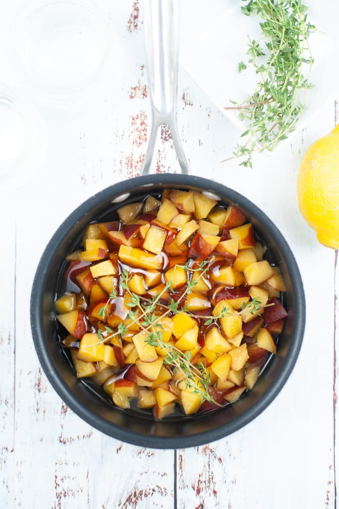 overhead shot of the ingredients for a peach honey simple syrup n a large pot with a sprig of fresh thyme on top