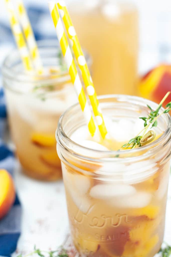 Fresh peach honey cocktail served in a glass mason jar with lots of ice, fresh peach slices and fresh thyme