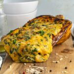 Front up close shot of melted four cheese mixture coming out of a roast stuffed butternut squash on a wooden board